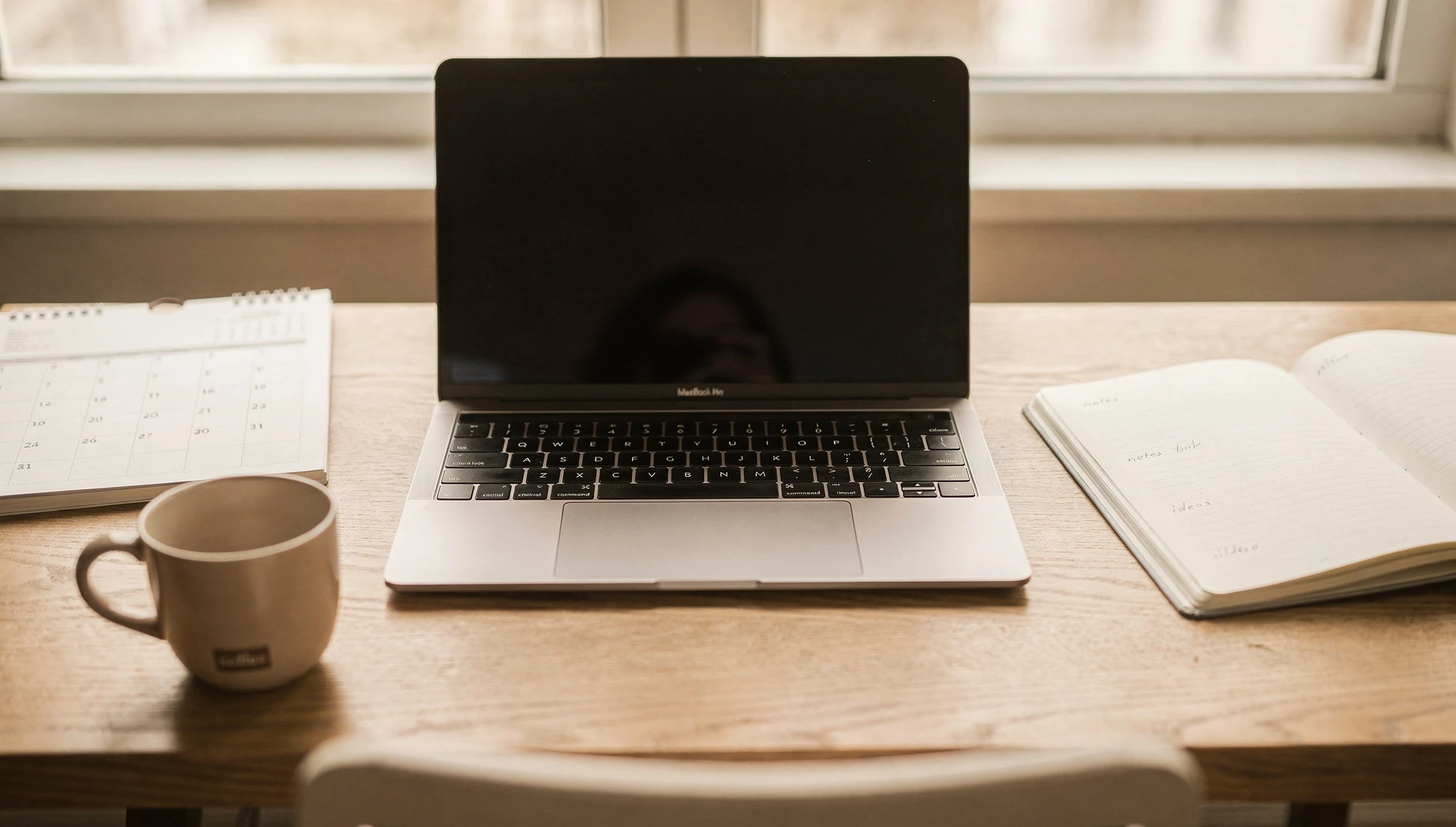 An open calendar and notebook on a desk with a laptop and coffee cup in soft natural light