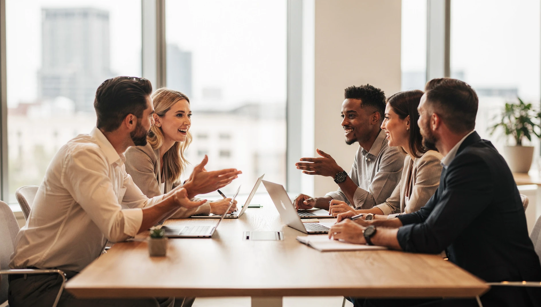 A small community of professionals gathered around a table in conversation in a warm collaborative atmosphere with bright natural light in a modern space