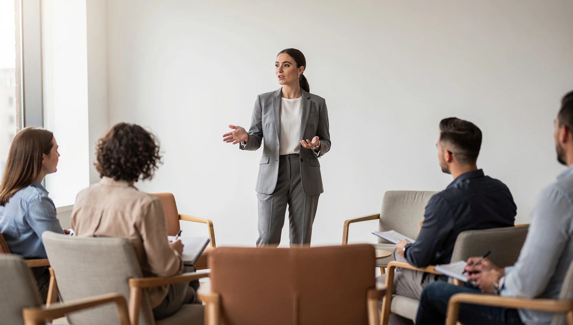 A person confidently presenting to a small group in a bright modern space with engaged audience