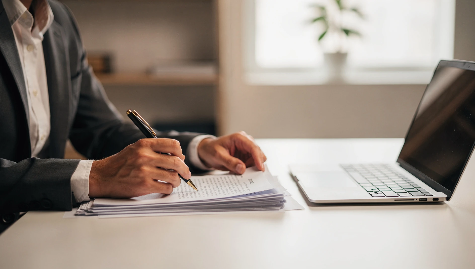 A professional reviewing legal documents at a clean desk with a pen and laptop in soft natural light