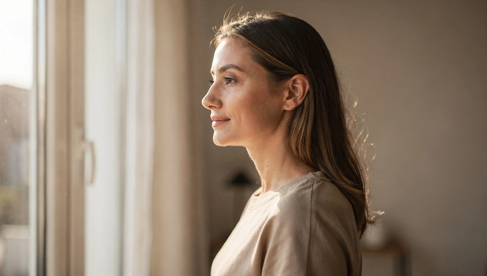A person standing at a window looking outward with quiet confidence in soft natural light