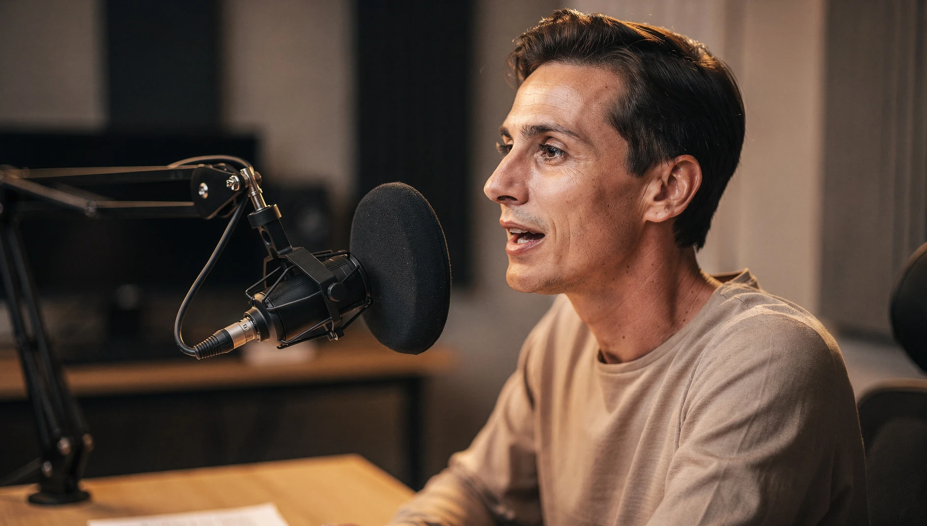 A professional speaking into a podcast microphone in a minimal recording setup with warm studio lighting