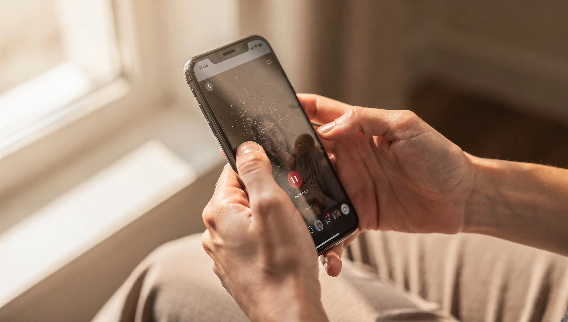 A close-up of a person scrolling through a smartphone profile page by a bright window in soft natural light