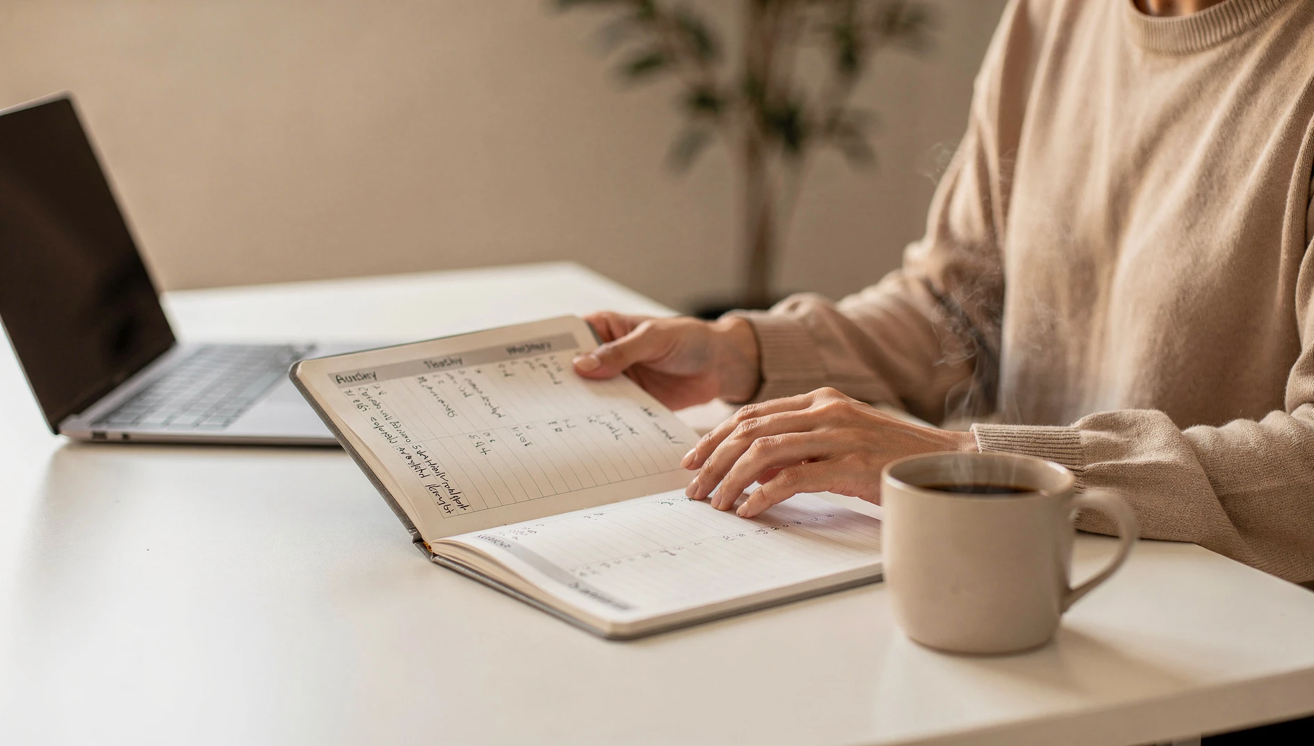 A professional reviewing a weekly planner at a clean desk with a laptop and coffee in morning natural light