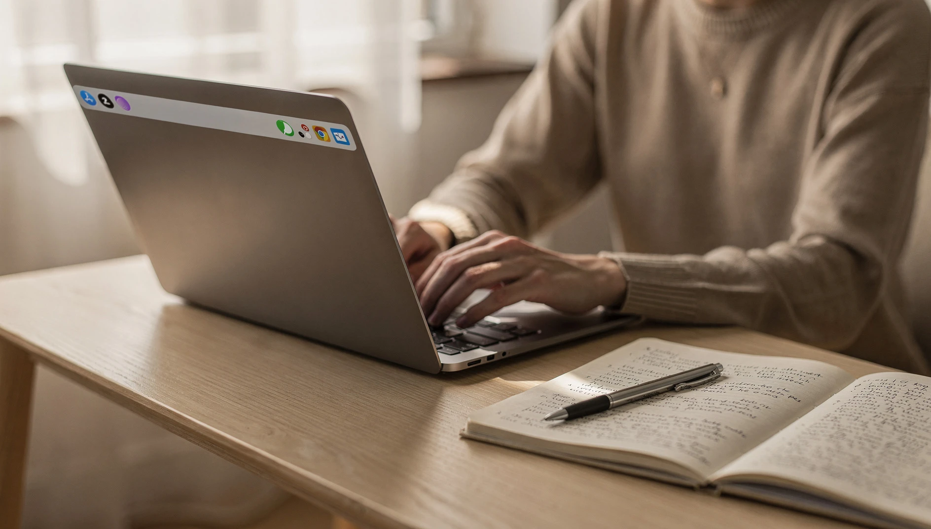 A person working at a laptop with handwritten notes on a pad beside them in warm window light