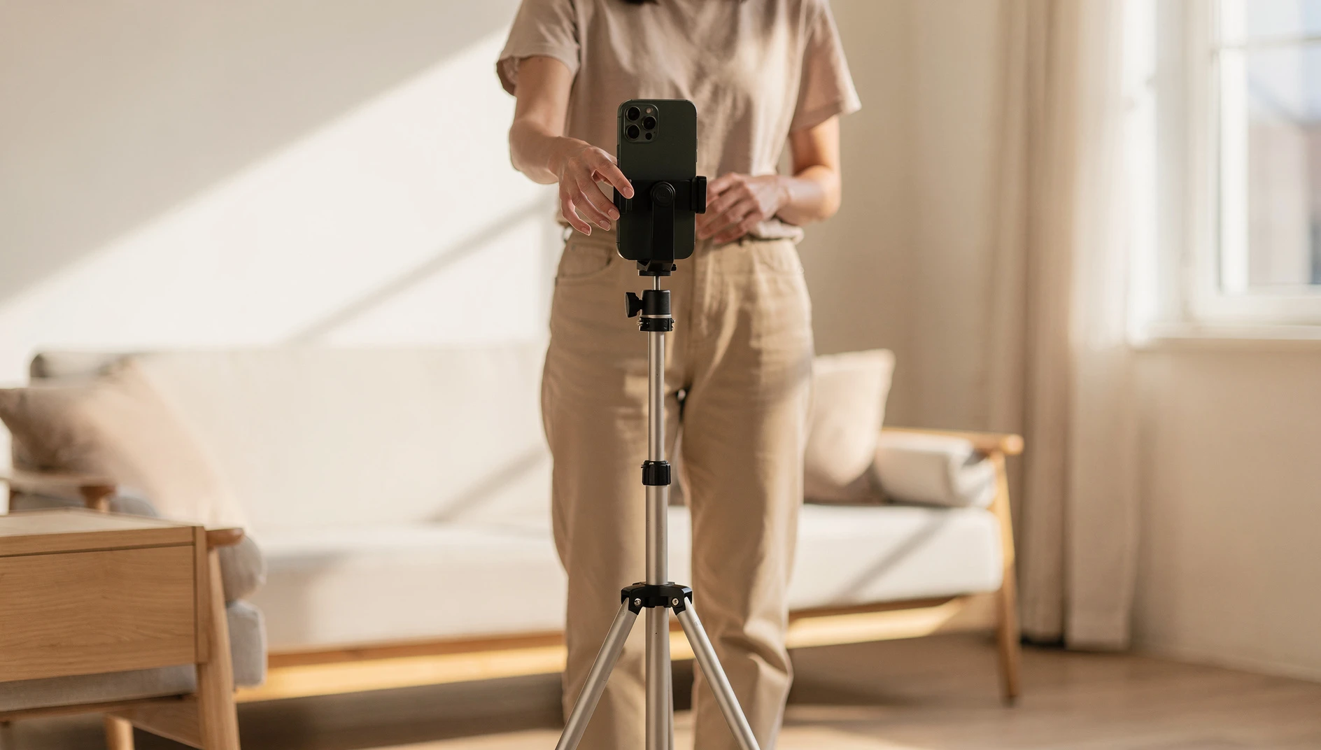 A person filming a vertical video on a phone mounted on a tripod in a bright modern room with soft natural light
