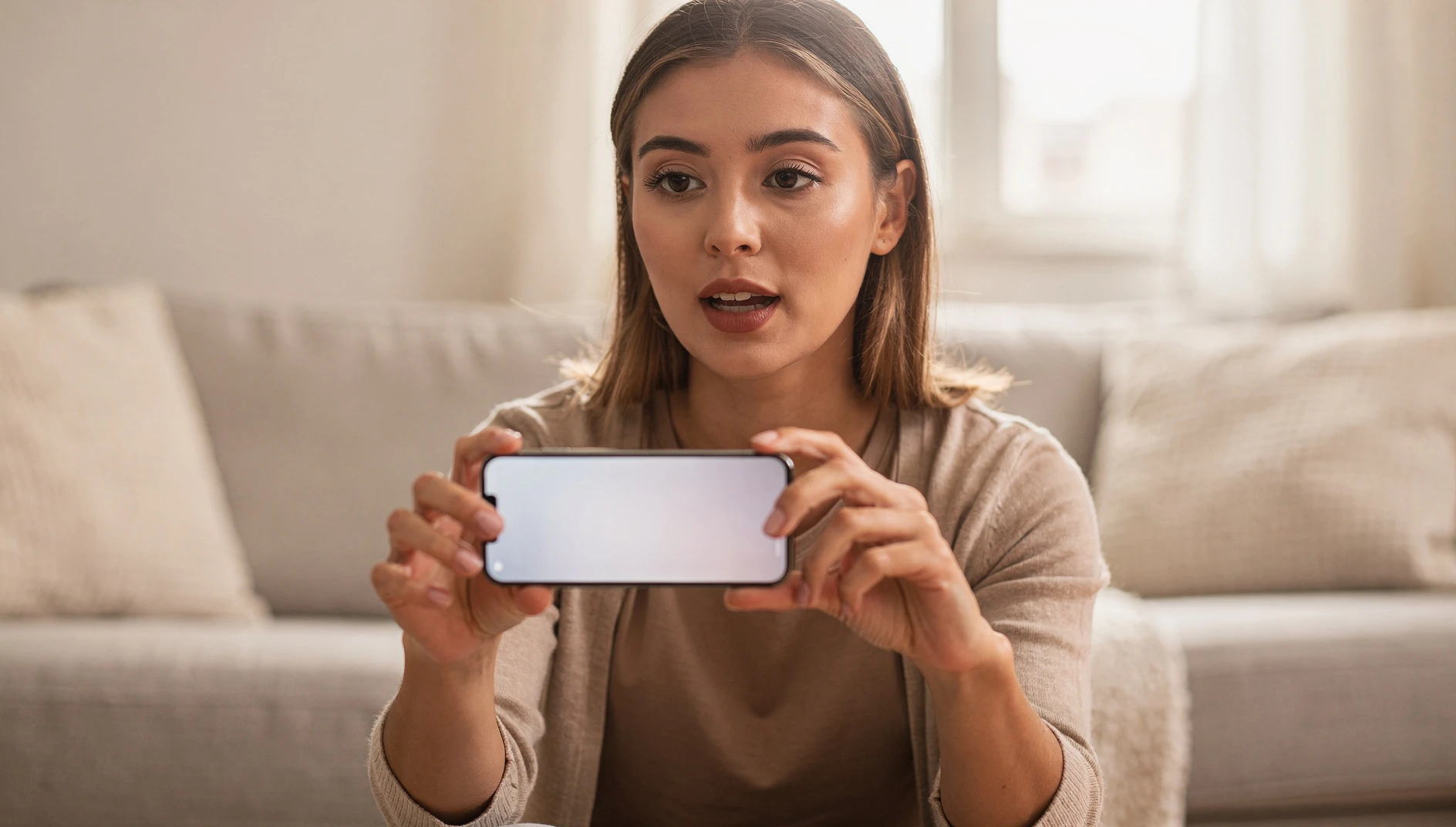 A person holding a smartphone horizontally with an engaged expression in a bright casual room setting