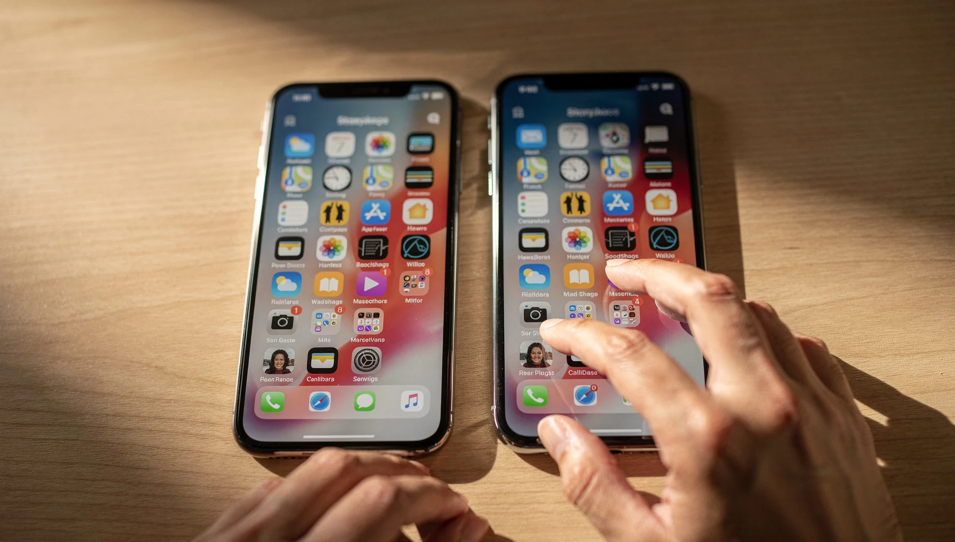 Two smartphones on a desk in warm natural light with hands reaching toward one of them